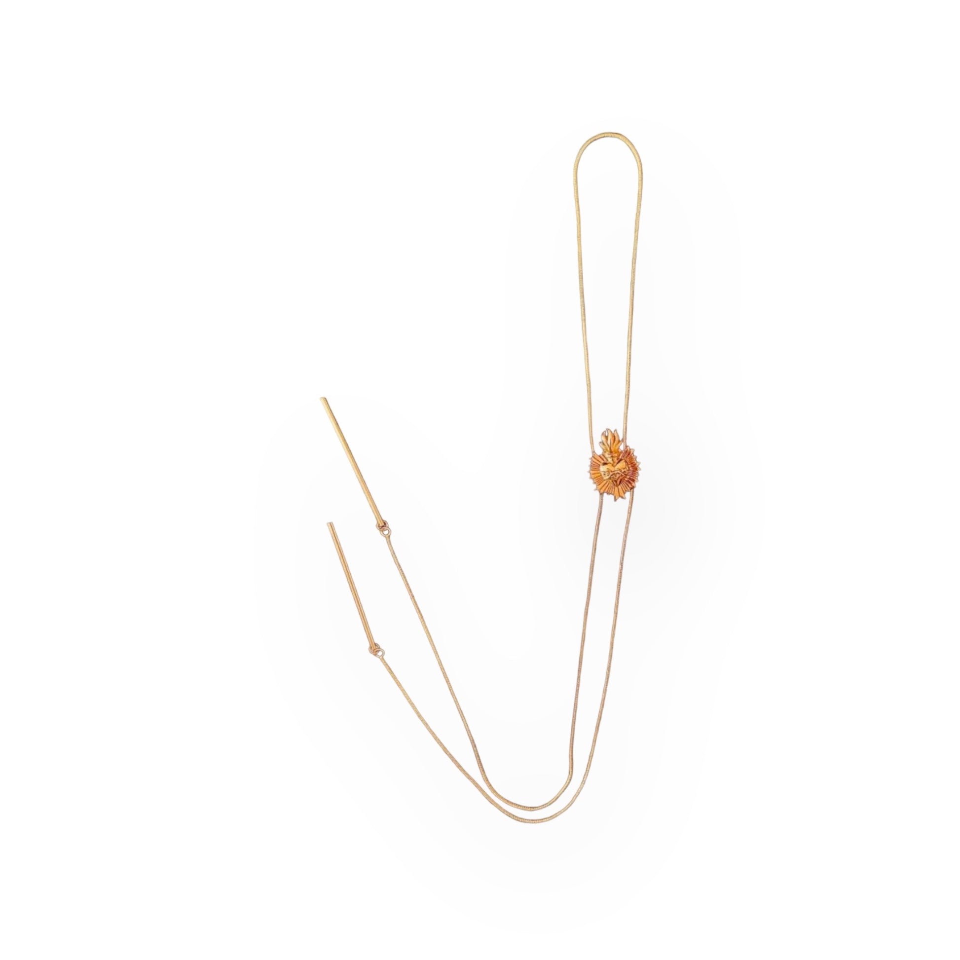 A gold bolo tie with a detailed centerpiece featuring a sacred heart design on a white background The tie has two long, delicate gold plated chains ending in slim metal bars