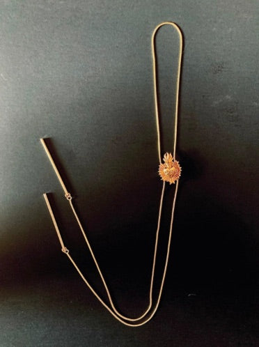A gold bolo tie with a detailed centerpiece featuring a radiant heart design on black background . The tie has two long, delicate gold plated chains ending in slim metal bars