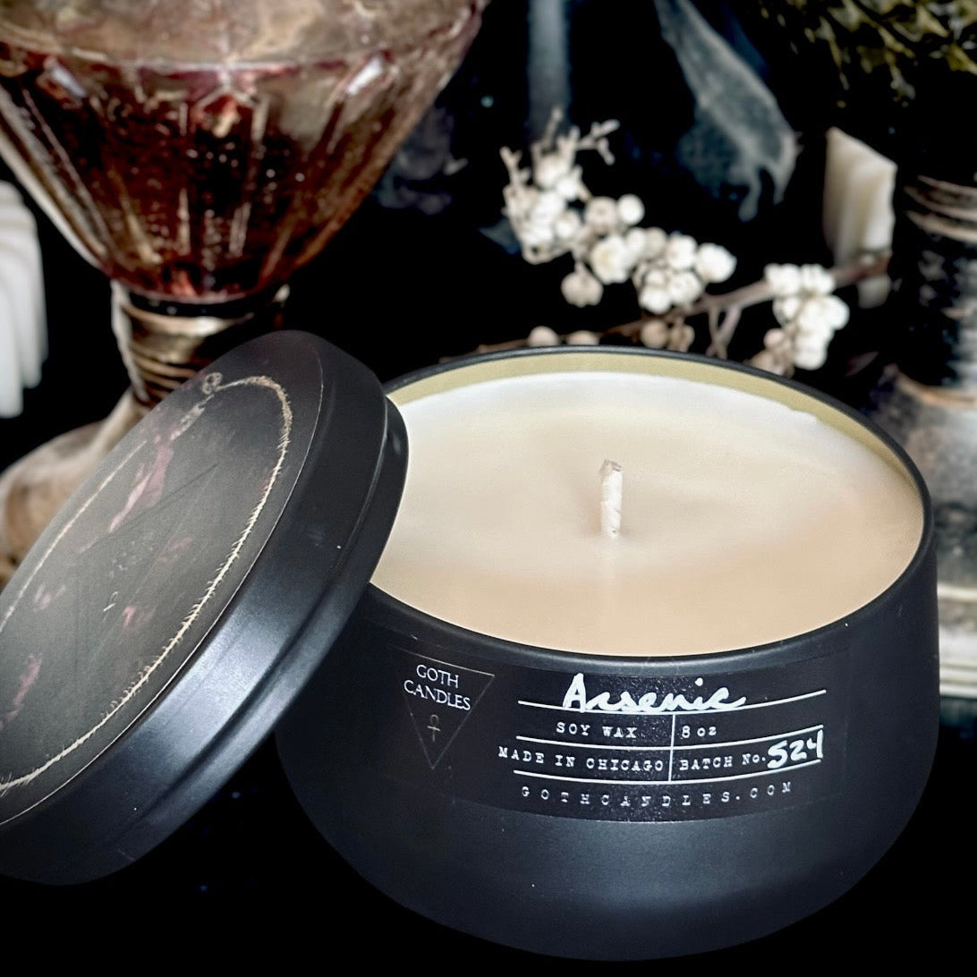 Black candle in a tin with a visible brand name on a dark background