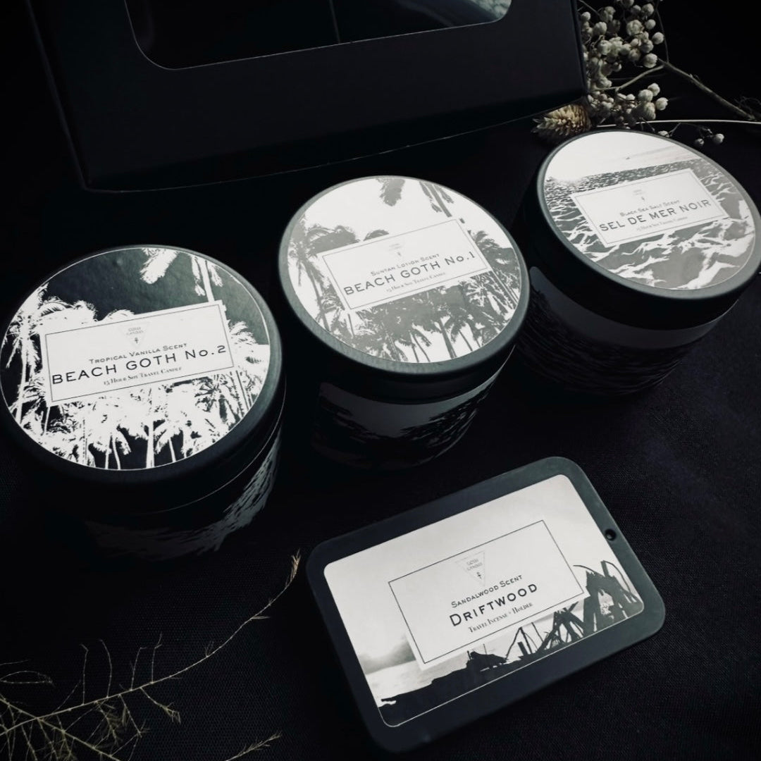 Three travel candle tins with labels on a dark surface