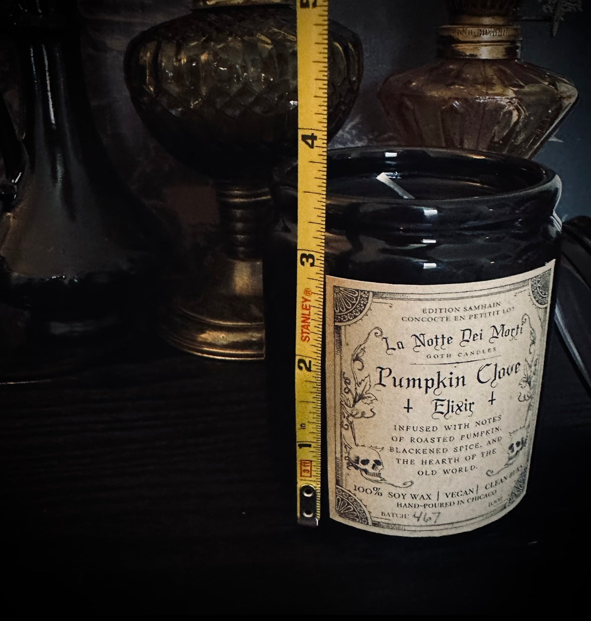 Black jar with a label on a dark background, featuring a measuring tape for scale.